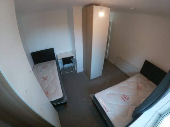 Bedroom with two single beds, desk, wardrobe, and gray carpet.