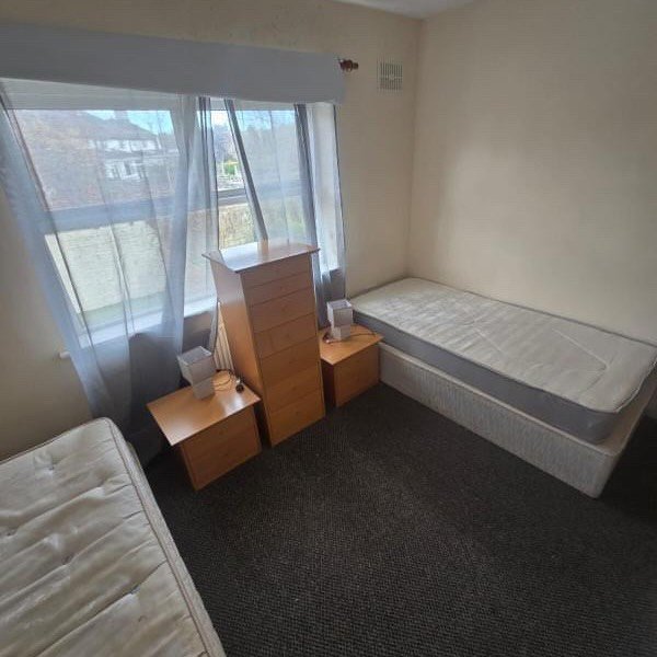 Bedroom with two single beds, tall dresser, and bedside tables. Neutral color scheme.