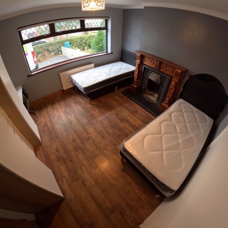 Bedroom with two single beds, fireplace, window, and wood floors. Neutral color scheme.