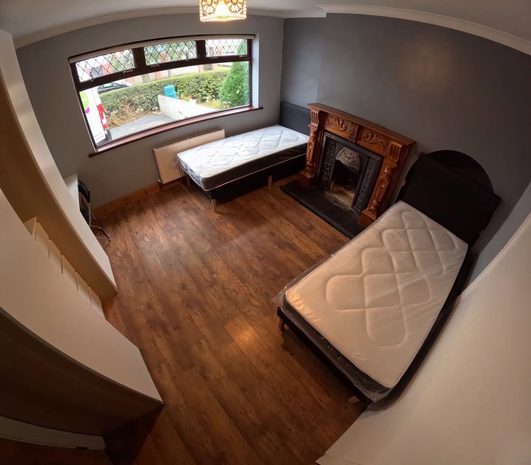 Bedroom with two single beds, fireplace, window, and wood floors. Neutral color scheme.