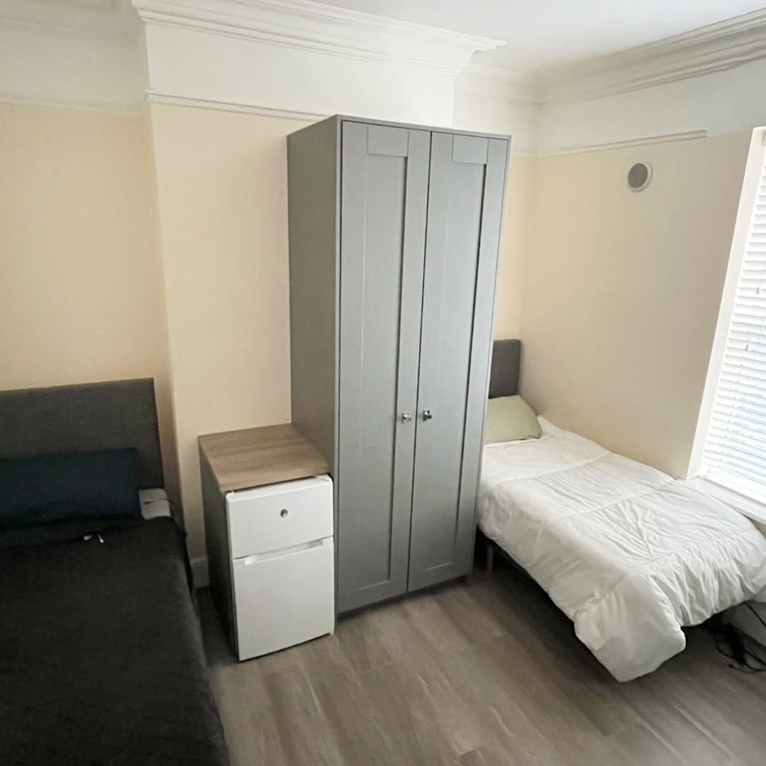 Bedroom with two single beds, gray wardrobe, and mini fridge. Interior design.