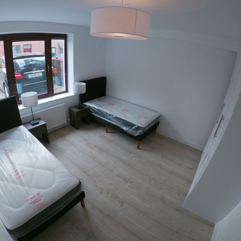 Bedroom with two single beds, bedside tables, wardrobe, and a window view of a car.