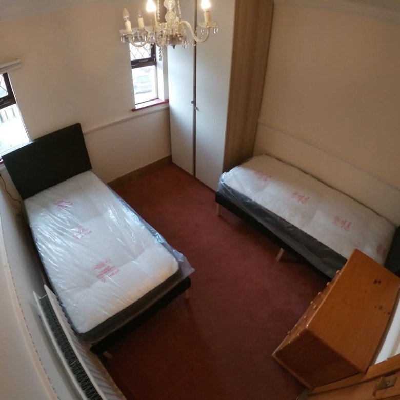 Bedroom with two single beds, wardrobe, chandelier, and window. Red carpet and neutral wall colors.