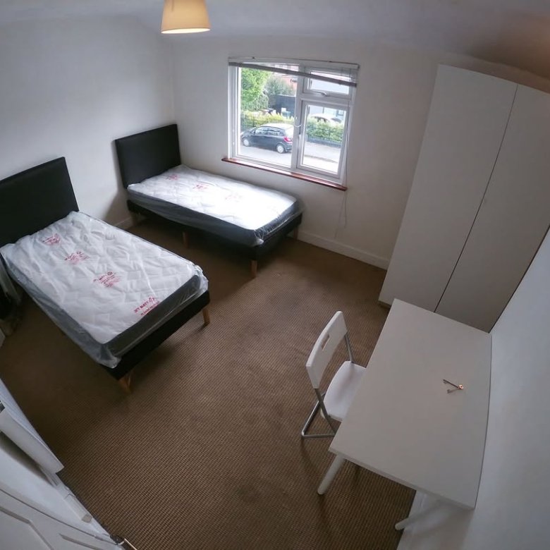 Bedroom with two single beds, wardrobe, desk, and chair near a window.