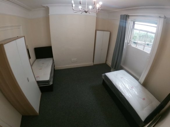 Bedroom with two single beds, wardrobes, gray carpet, and natural light from a window.