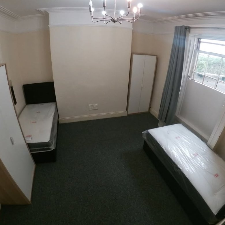 Bedroom with two single beds, wardrobes, gray carpet, and natural light from a window.