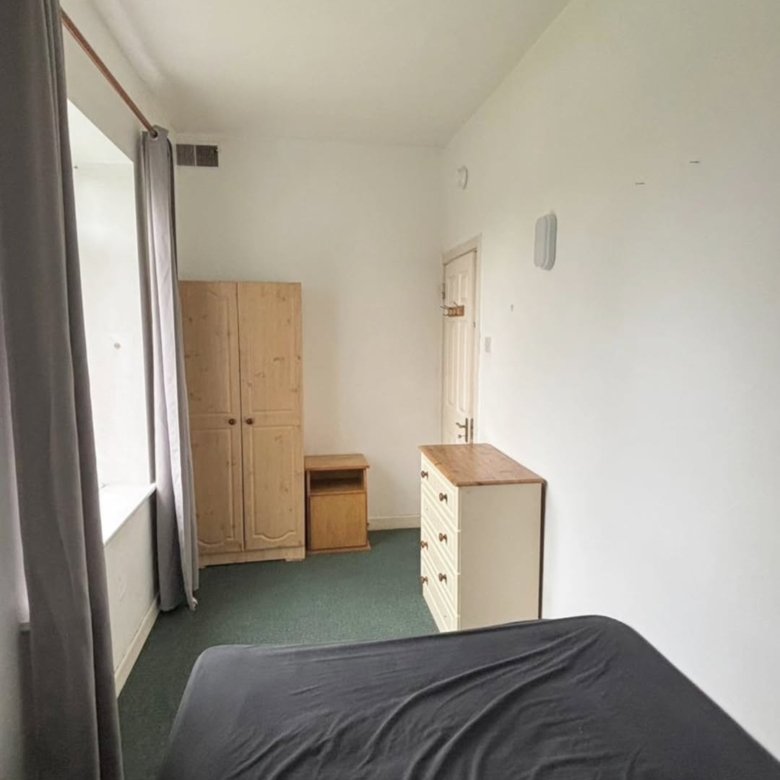 Bedroom with wardrobe, chest of drawers, green carpet, and grey curtains.