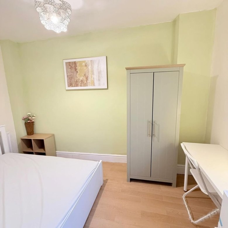 Bedroom with bed, wardrobe, desk, and artwork on green wall. Bright interior.