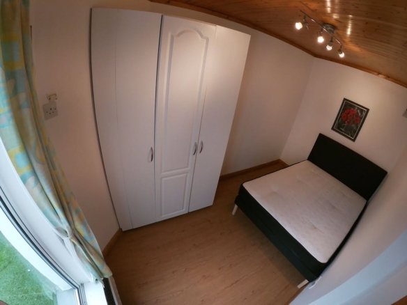 Bedroom with white wardrobe, bed, and window with patterned curtain.