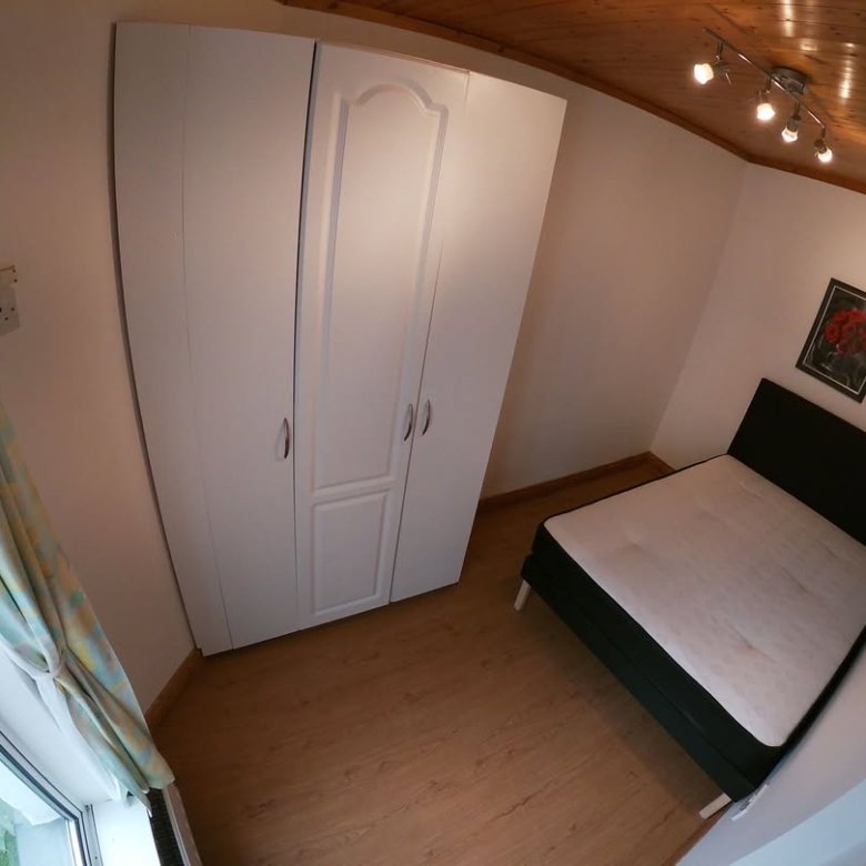 Bedroom with white wardrobe, bed, and window with patterned curtain.