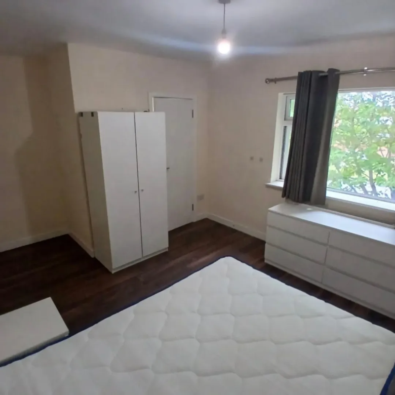 Bedroom with white wardrobe, chest of drawers, and double bed under a window.