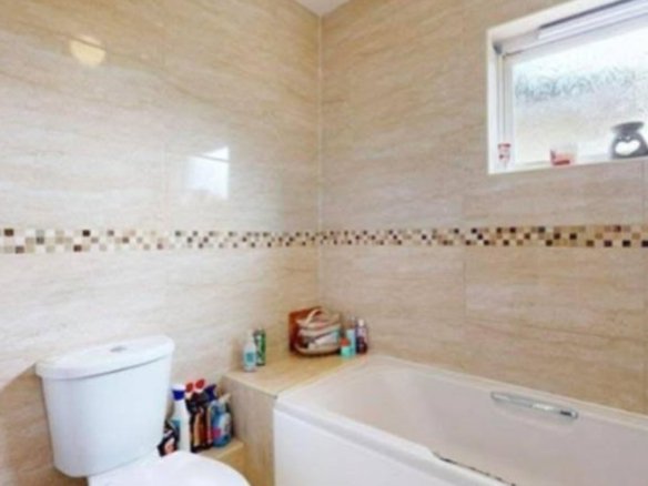 Bathroom with beige tile, white toilet and bathtub, and decorative mosaic border.