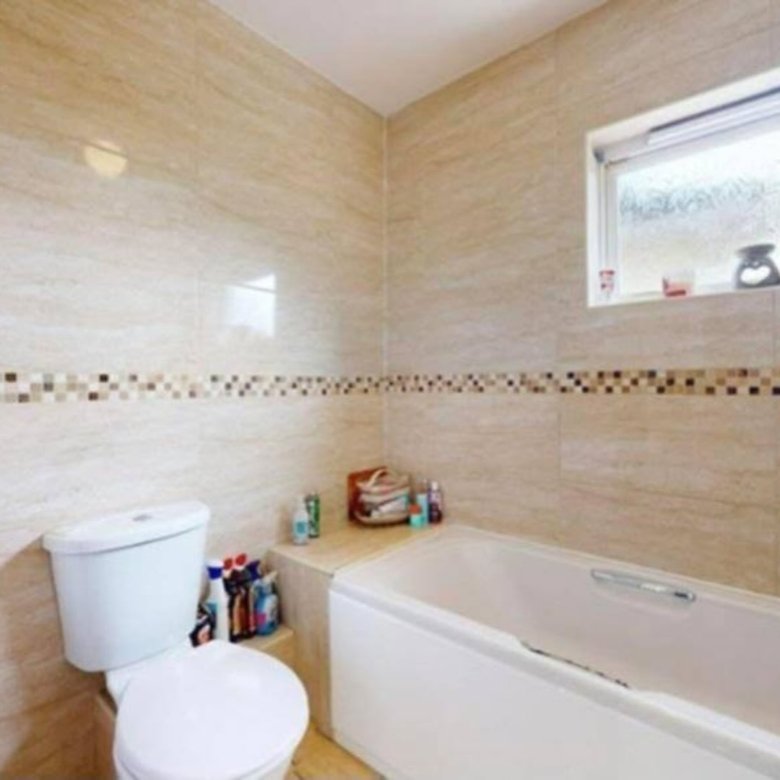 Bathroom with beige tile, white toilet and bathtub, and decorative mosaic border.