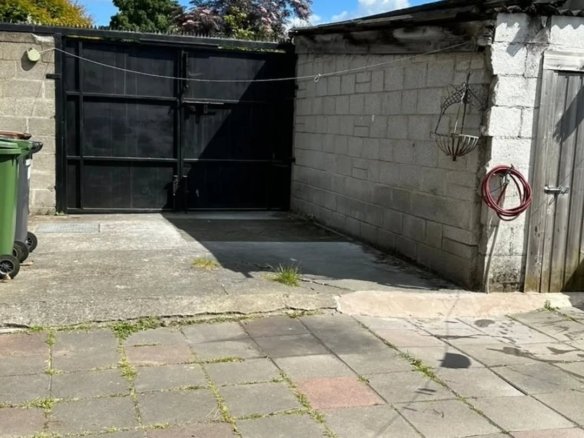 Black metal gate, concrete block wall, and paved patio under a blue sky with white clouds.