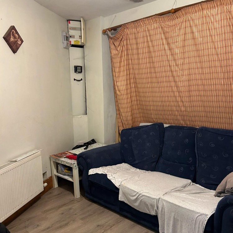 Living room interior with blue sofa, radiator, and electrical panel on wall.