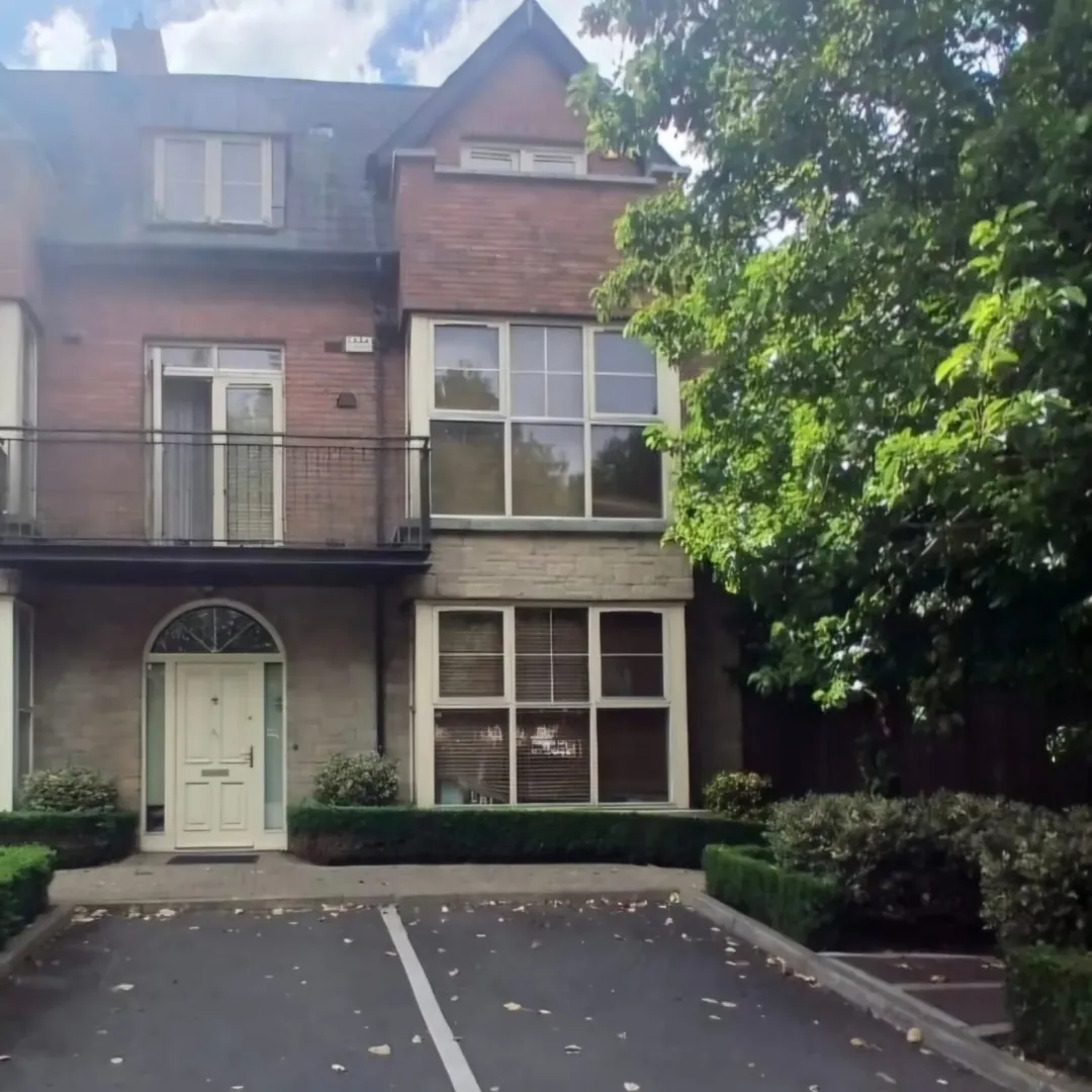 Brick building with white door and windows, balcony, and green landscaping.