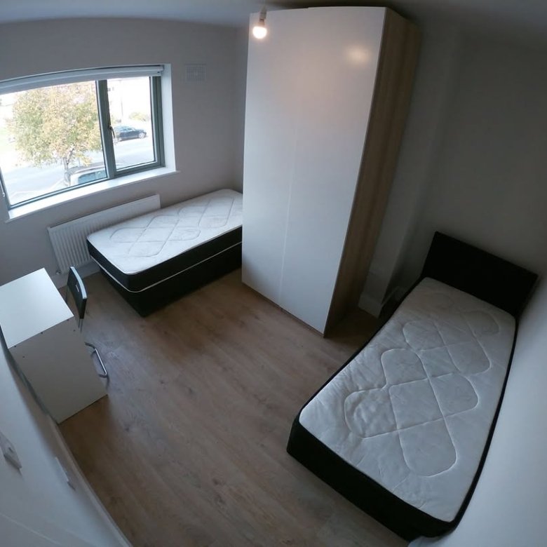 Bright room with two beds, wardrobe, desk, and window. Clean, modern interior.