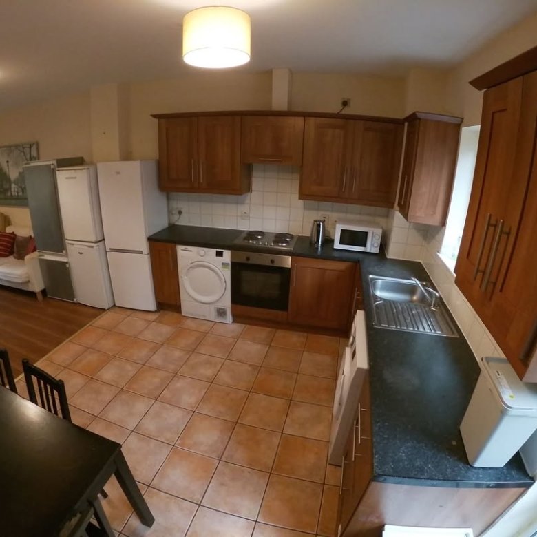 Bright kitchen with appliances, dining table, and living area. Wood cabinets, tile floor.