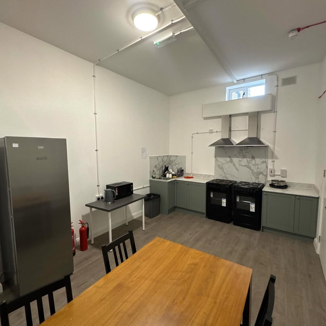 Bright kitchen with sage green cabinets, stainless steel fridge, oven, and wooden dining table.