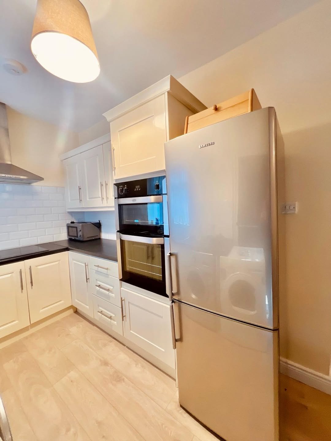 Bright kitchen with stainless steel fridge, white cabinets, and wood floor.