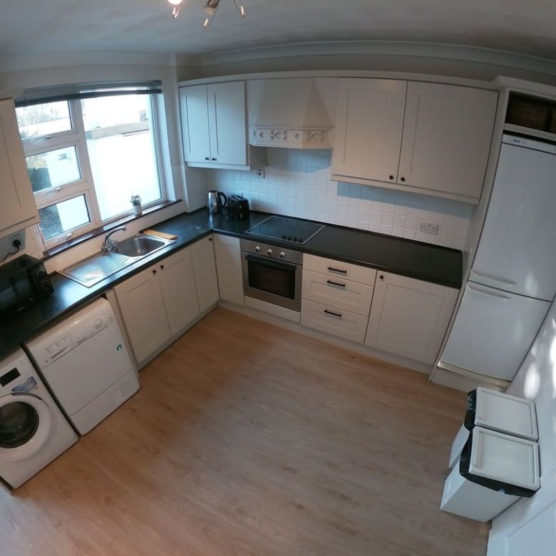 Bright kitchen with white cabinets, black countertops, washing machine, and wood flooring.