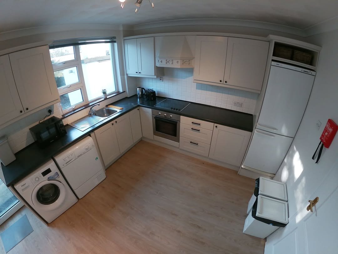 Bright kitchen with white cabinets, black countertops, washing machine, and wood flooring.