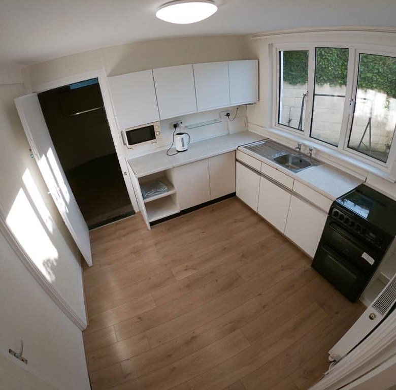 Bright kitchen with white cabinets, wood floor, window, and black stove.