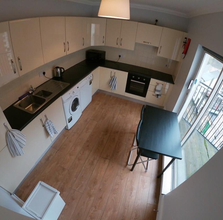 Bright kitchen with white cabinets, wood floor, black countertop, dining table, and window to balcony.