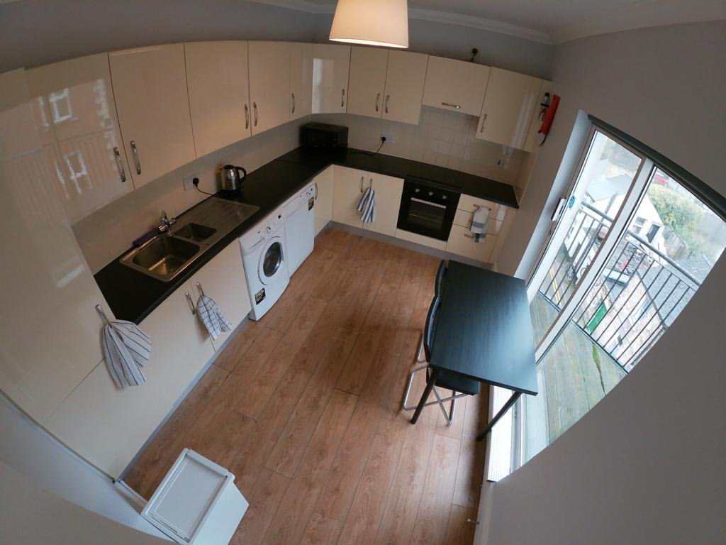 Bright kitchen with white cabinets, wood floor, black countertop, dining table, and window to balcony.
