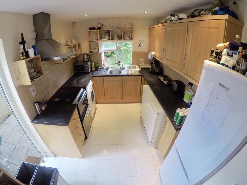 Bright kitchen with light wood cabinets, black countertops, and white tile floor.