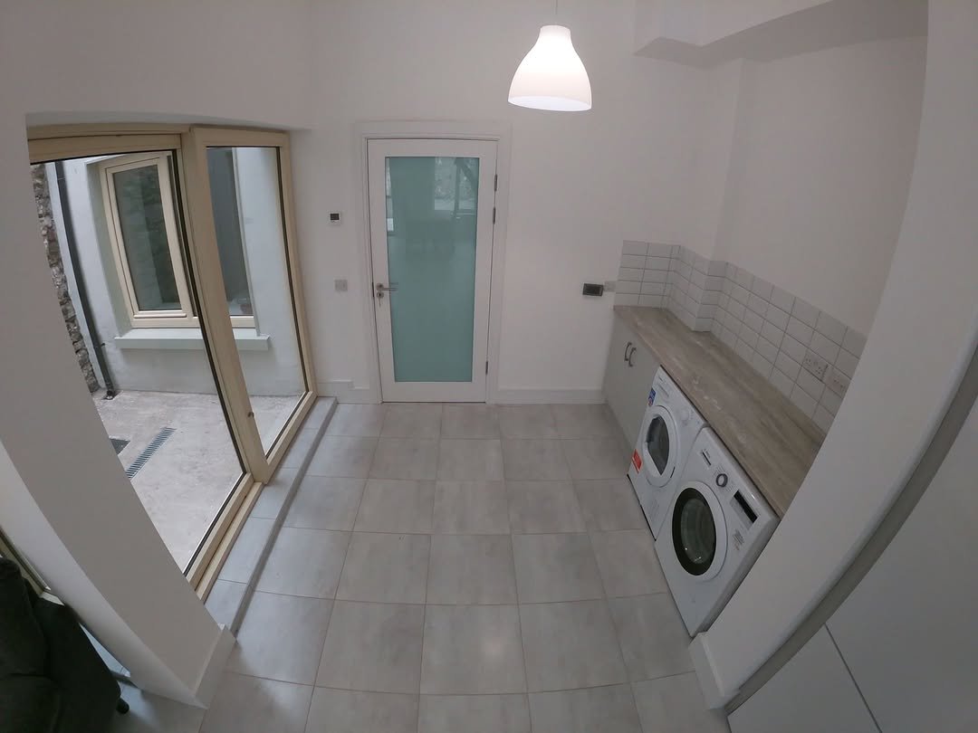 Bright laundry room with washer, dryer, door to patio, and white cabinets.
