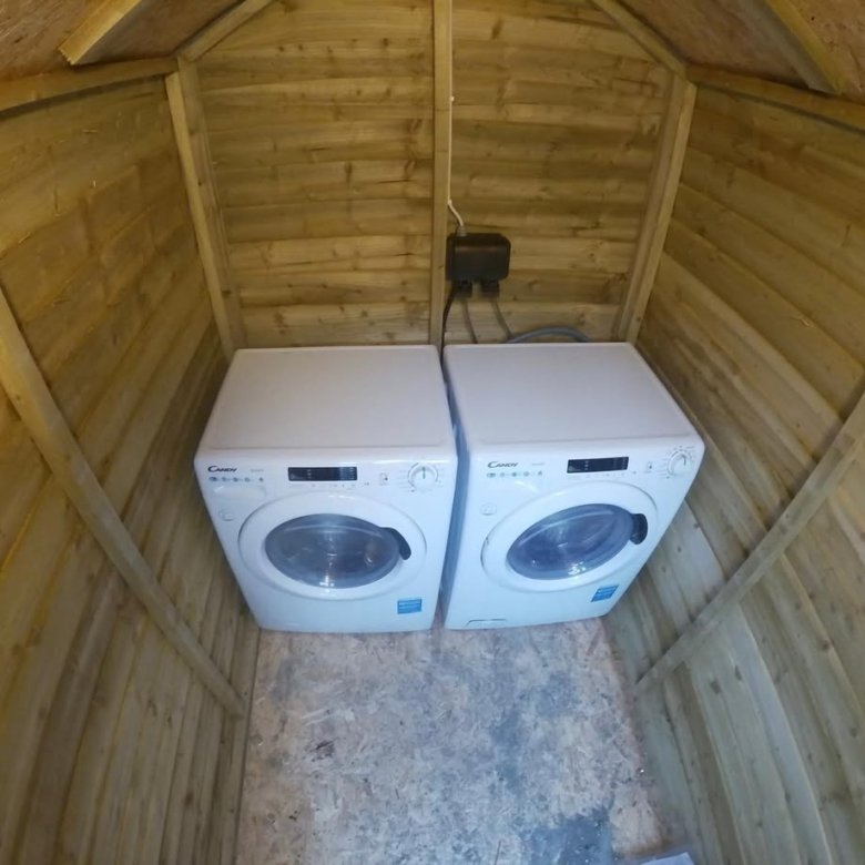 Two white Candy washing machines inside a wooden shed, connected to a black electrical box.