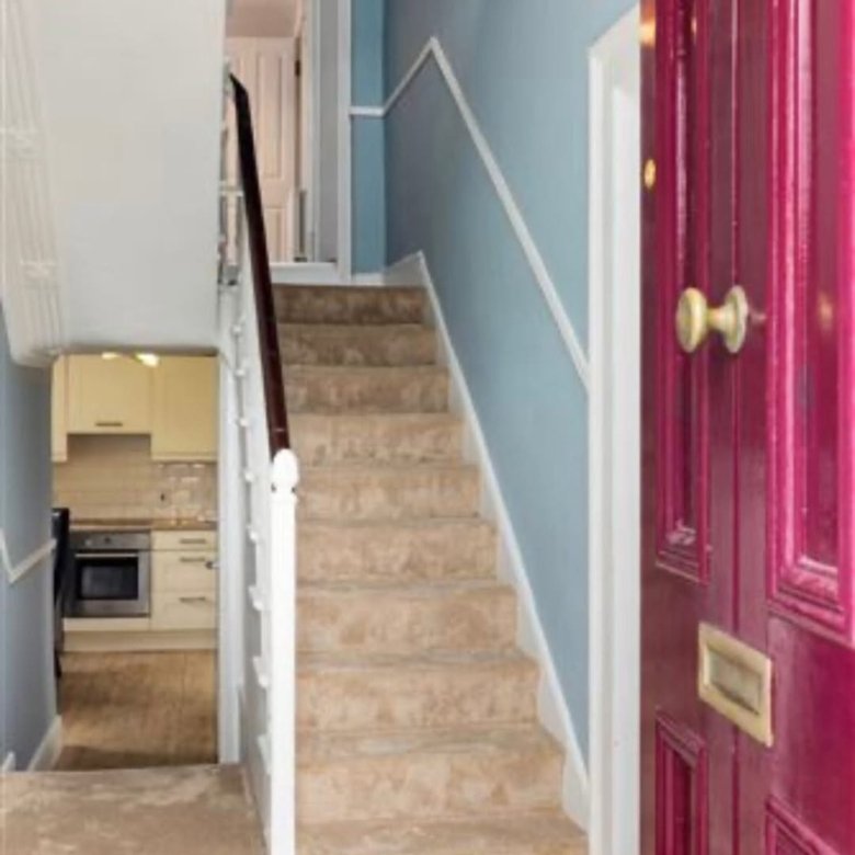 Entryway with carpeted stairs, blue walls, white trim, and a burgundy front door.