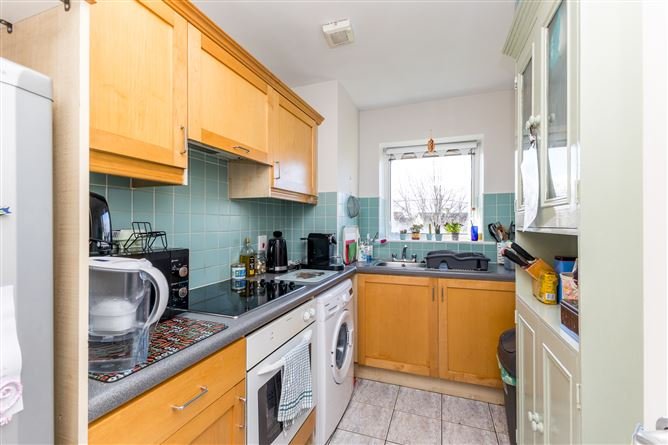 Compact kitchen with light wood cabinets, blue tile backsplash, and appliances under a window.