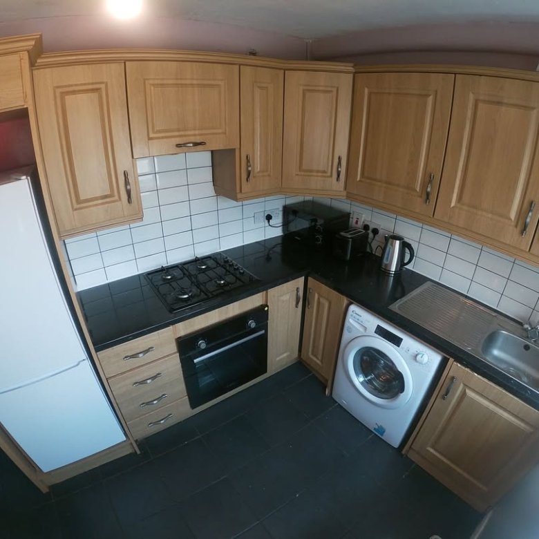 Compact kitchen with oak cabinets, black countertops, and appliances.