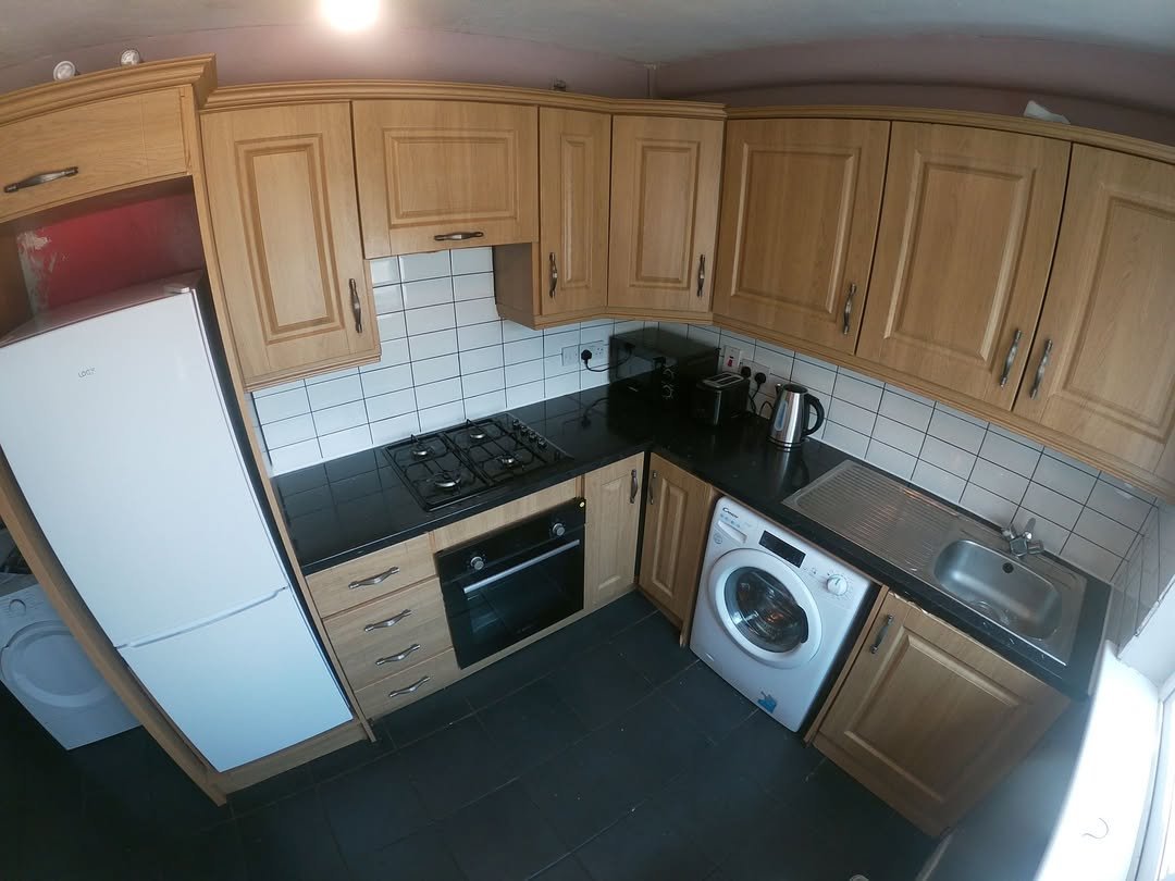 Compact kitchen with oak cabinets, black countertops, and appliances.