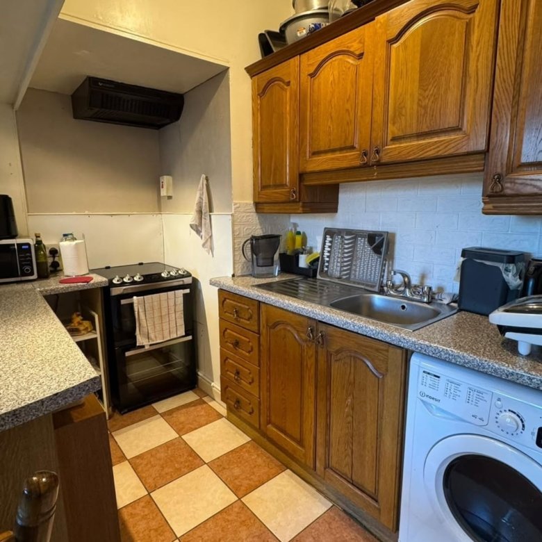 Compact kitchen with oak cabinets, checkered flooring, and white washing machine.
