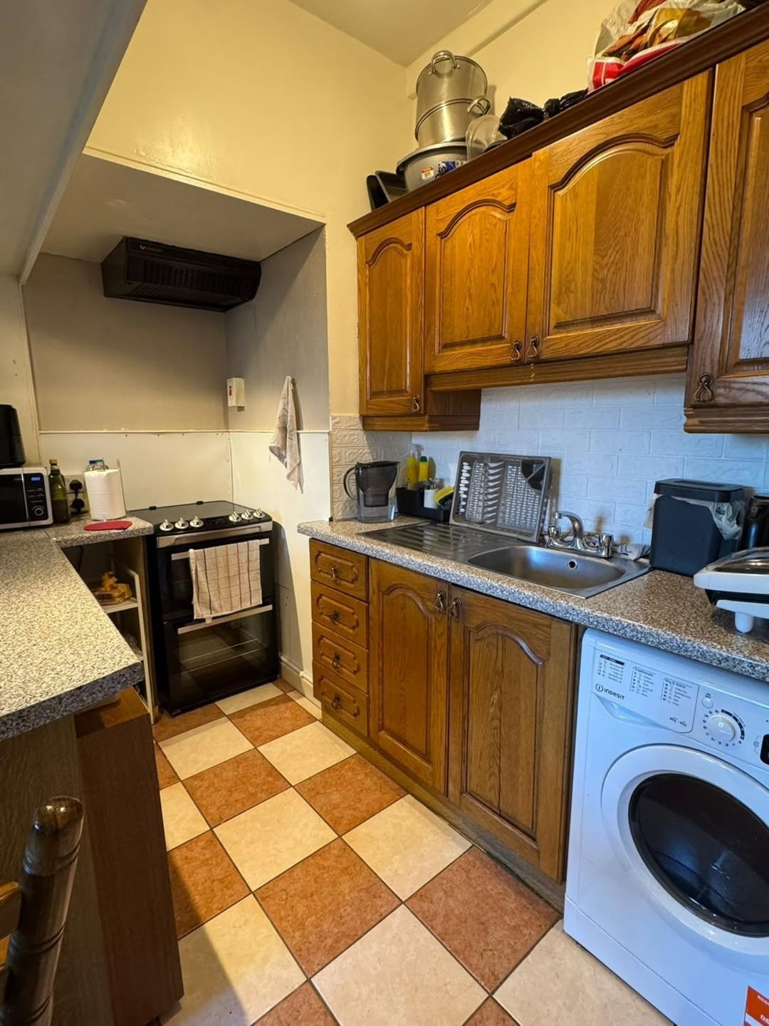 Compact kitchen with oak cabinets, checkered flooring, and white washing machine.