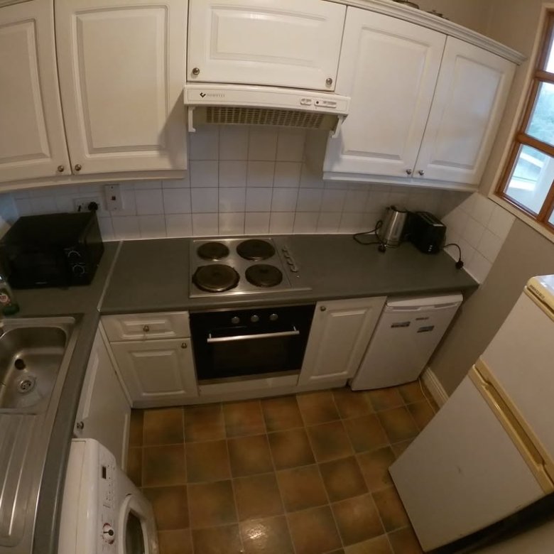 Compact kitchen with white cabinets, gray countertops, stove, and refrigerator.