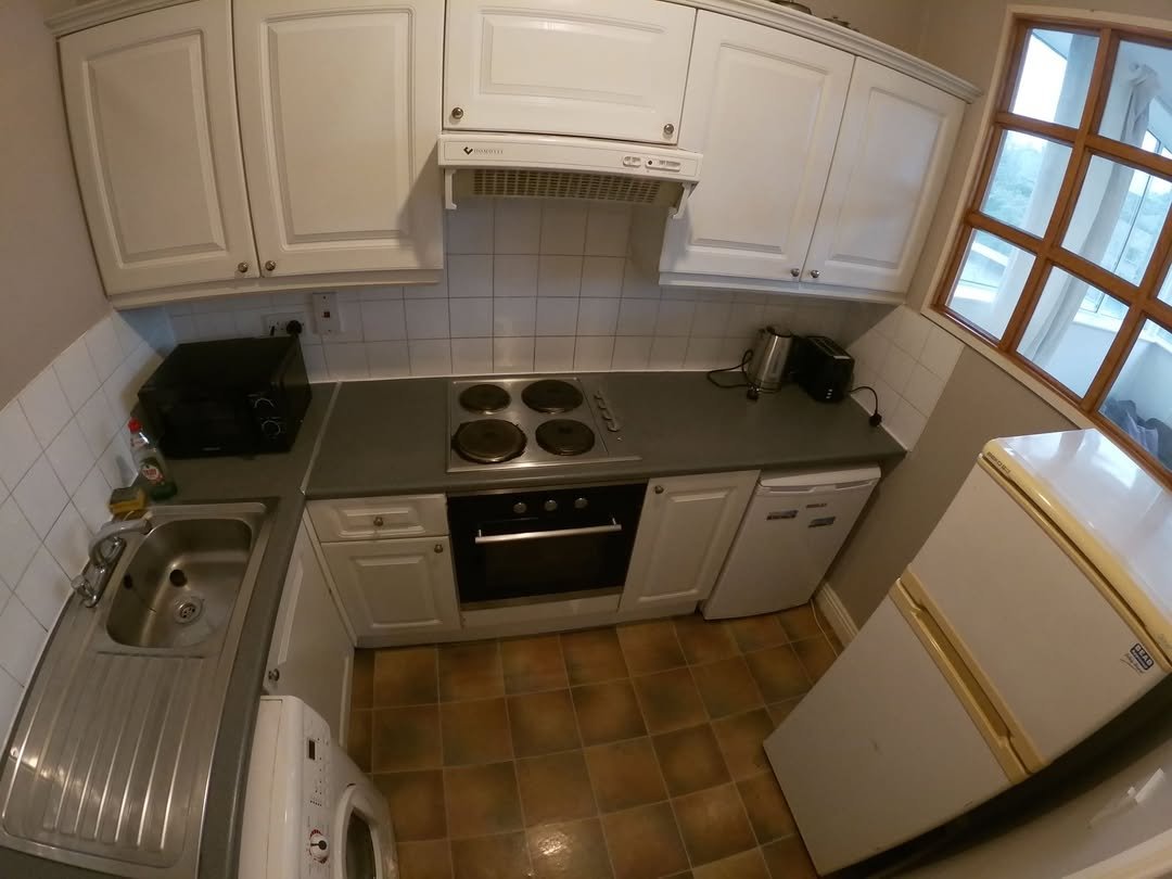 Compact kitchen with white cabinets, gray countertops, stove, and refrigerator.