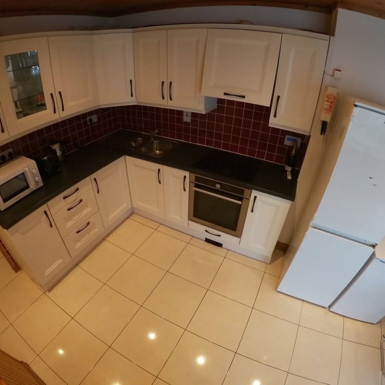 Compact kitchen with white cabinets, dark countertops, and red tile backsplash.