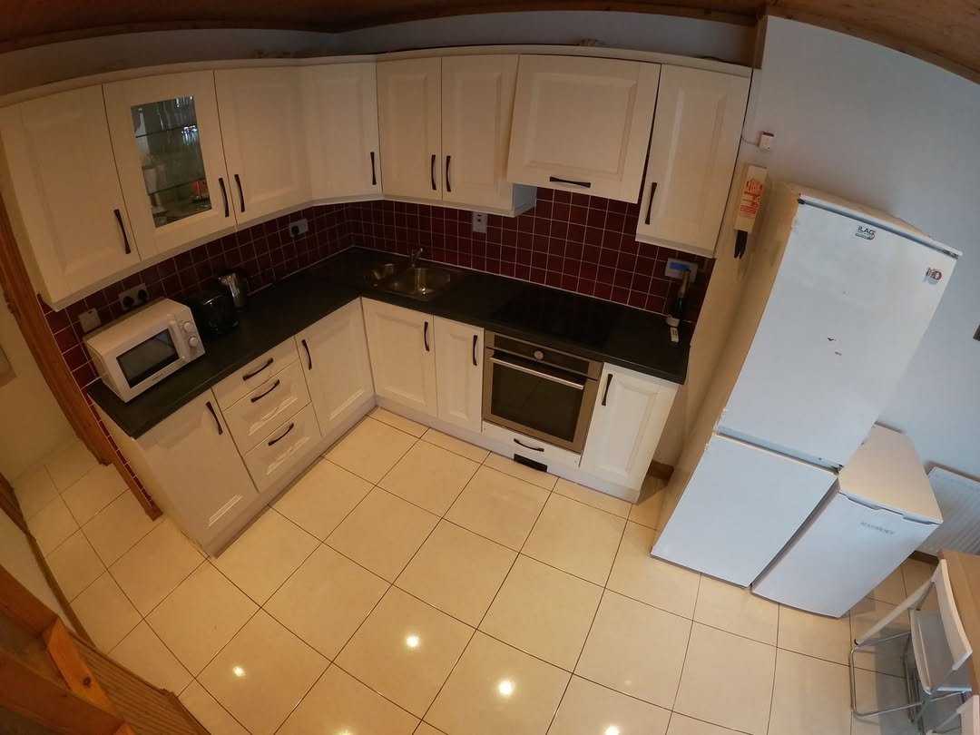 Compact kitchen with white cabinets, dark countertops, and red tile backsplash.