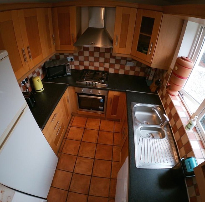 Compact kitchen with wood cabinets, black countertops, tile floor, and white refrigerator.