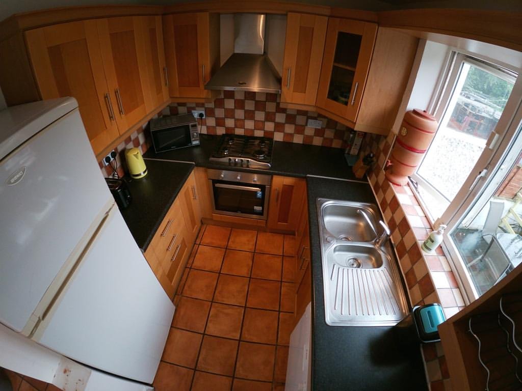 Compact kitchen with wood cabinets, black countertops, tile floor, and white refrigerator.