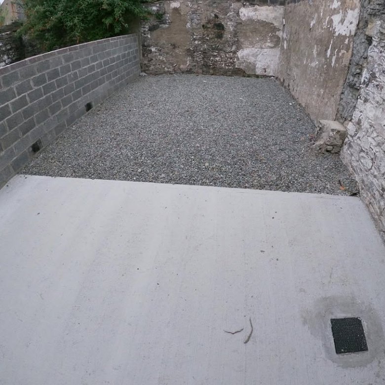 Outdoor concrete patio with gravel infill between walls, drainage squares visible.
