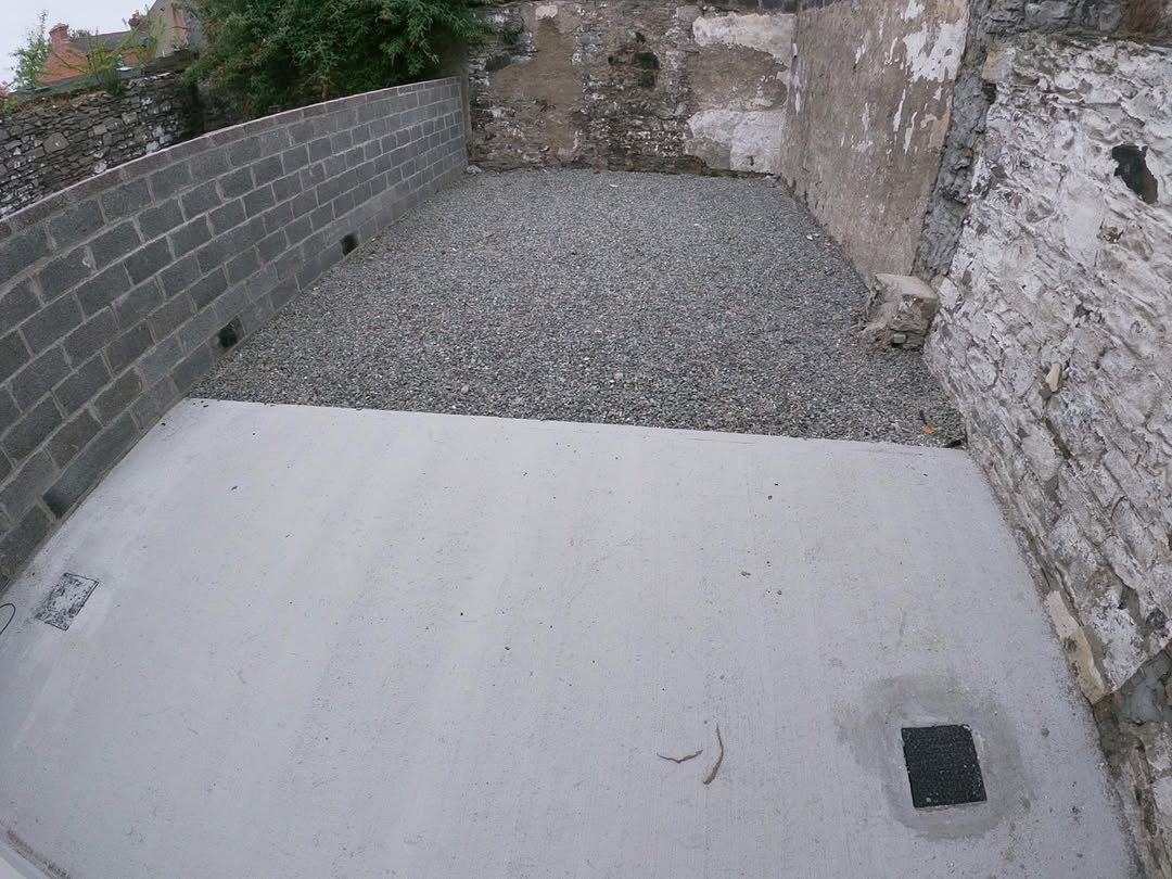 Outdoor concrete patio with gravel infill between walls, drainage squares visible.