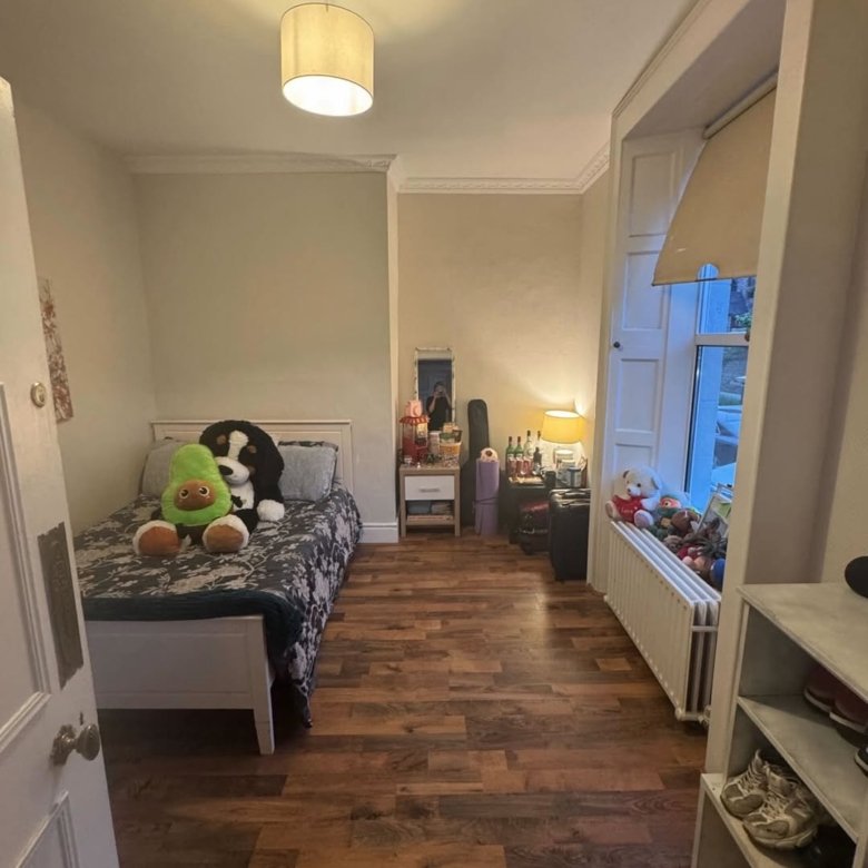 Cozy bedroom with single bed, window seat, and warm lighting. Stuffed animals add a playful touch.
