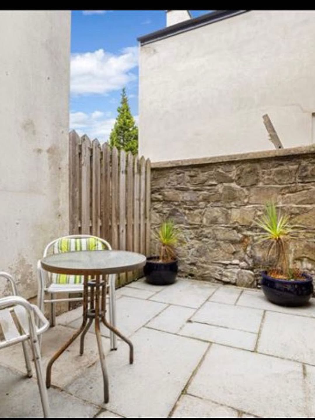 Cozy patio with stone wall, table, and plants in pots.