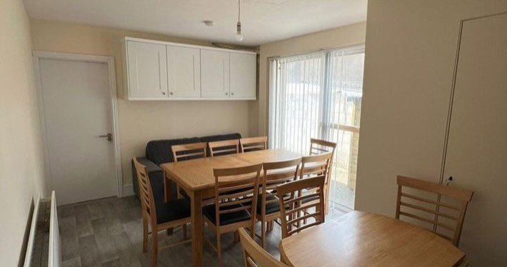 Dining area with table, chairs, and sofa under white cabinets, near sliding glass doors.