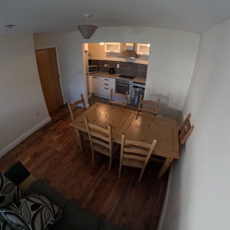 Dining area with wooden table and chairs, open kitchen in background.